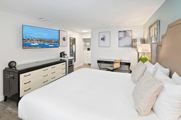 A hotel room with a large bed, a desk, a chair, a TV, and artwork on the walls.