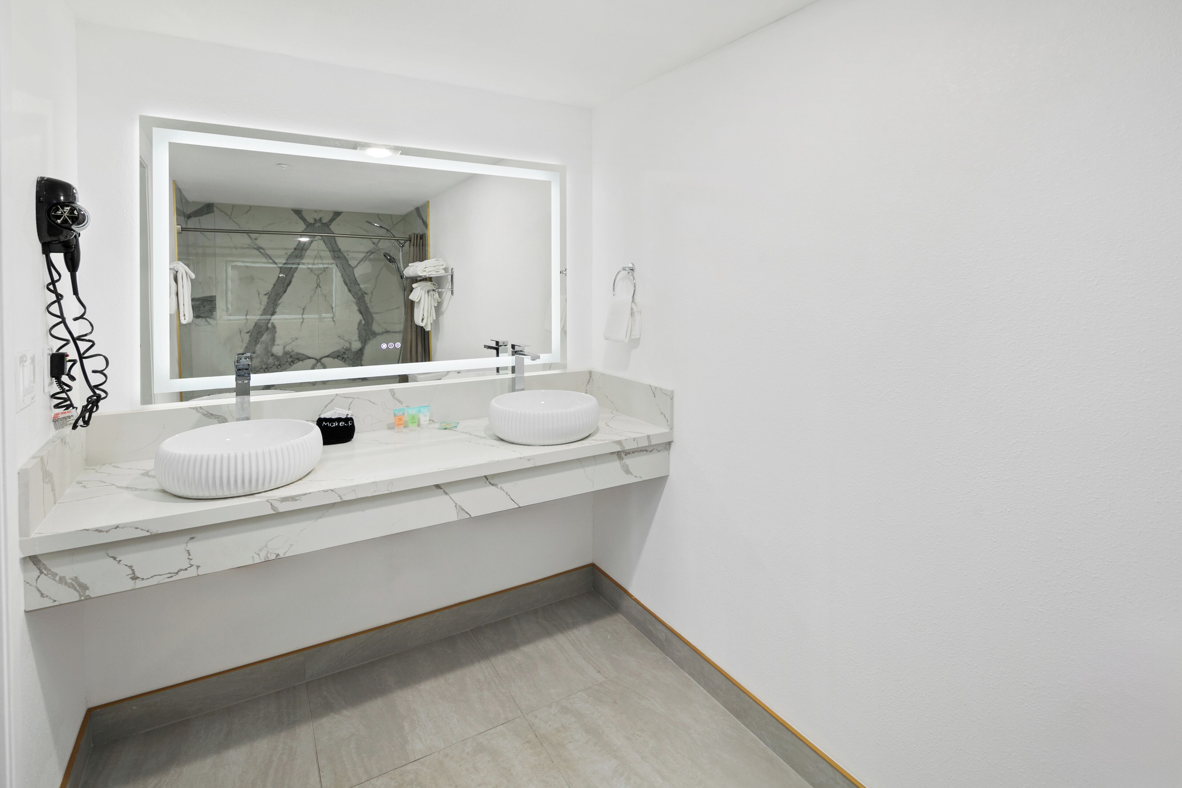 A modern bathroom with a large mirror, two sinks, and a hairdryer on the wall.