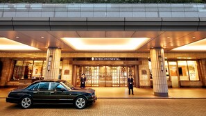 A grand entrance with a black car parked in front, a sign reading "Intercontinental," and two uniformed individuals standing by the entrance.