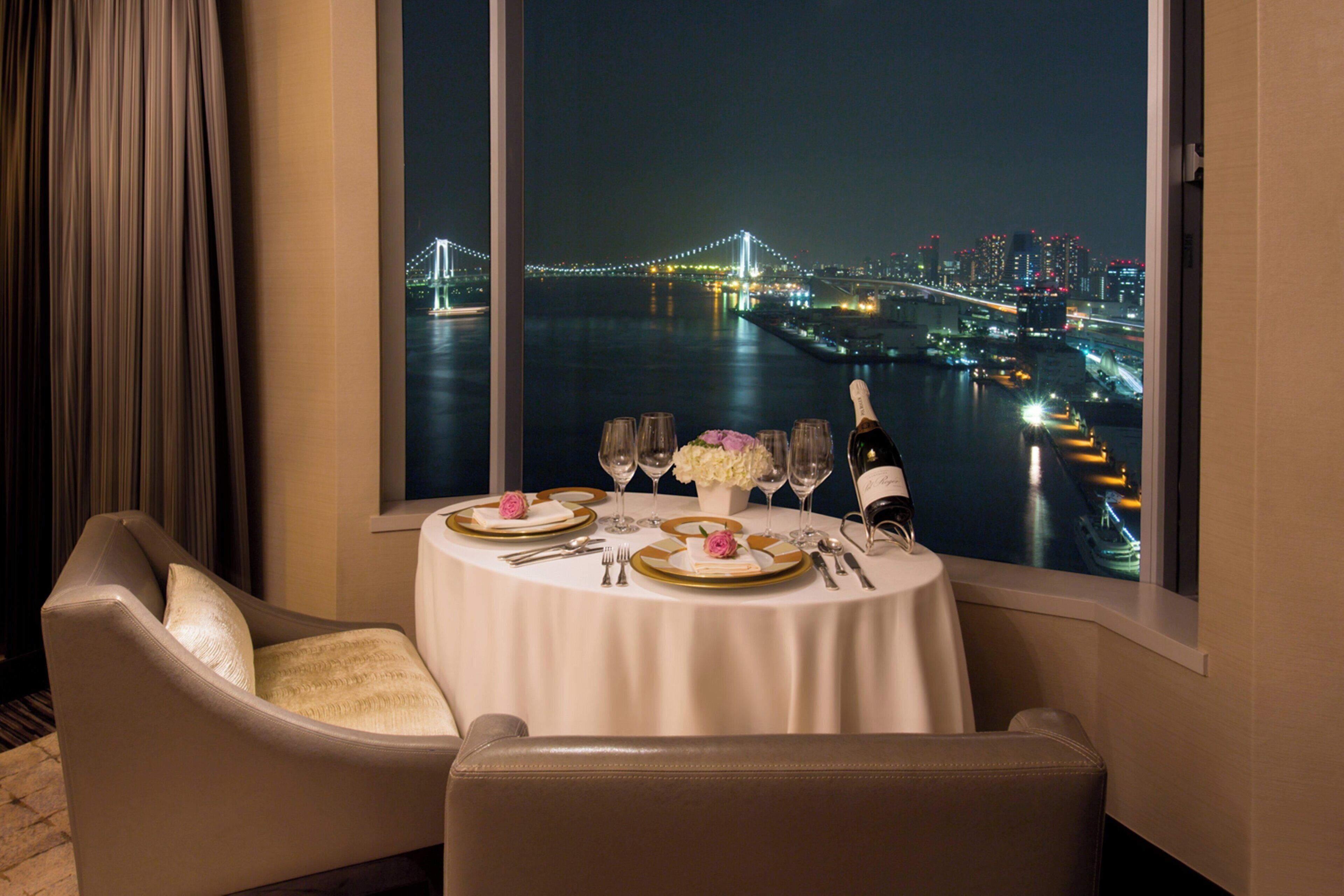 Mesa para dos servida con vista a un paisaje urbano y un puente, de noche.