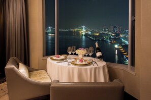 A dining table set for two with a view of a cityscape and a bridge at night. - InterContinental Tokyo Bay by IHG (Tokyo)