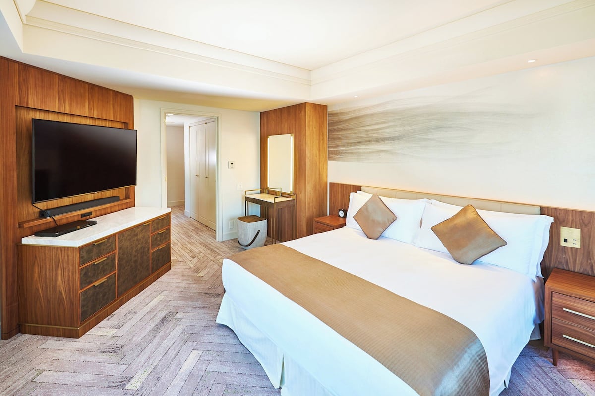 Hotellihuone, jossa on suuri sänky, puuhuonekalut, taulutelevisio ja peili.