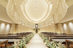 An interior with a central aisle, wooden pews, and a patterned wall design.