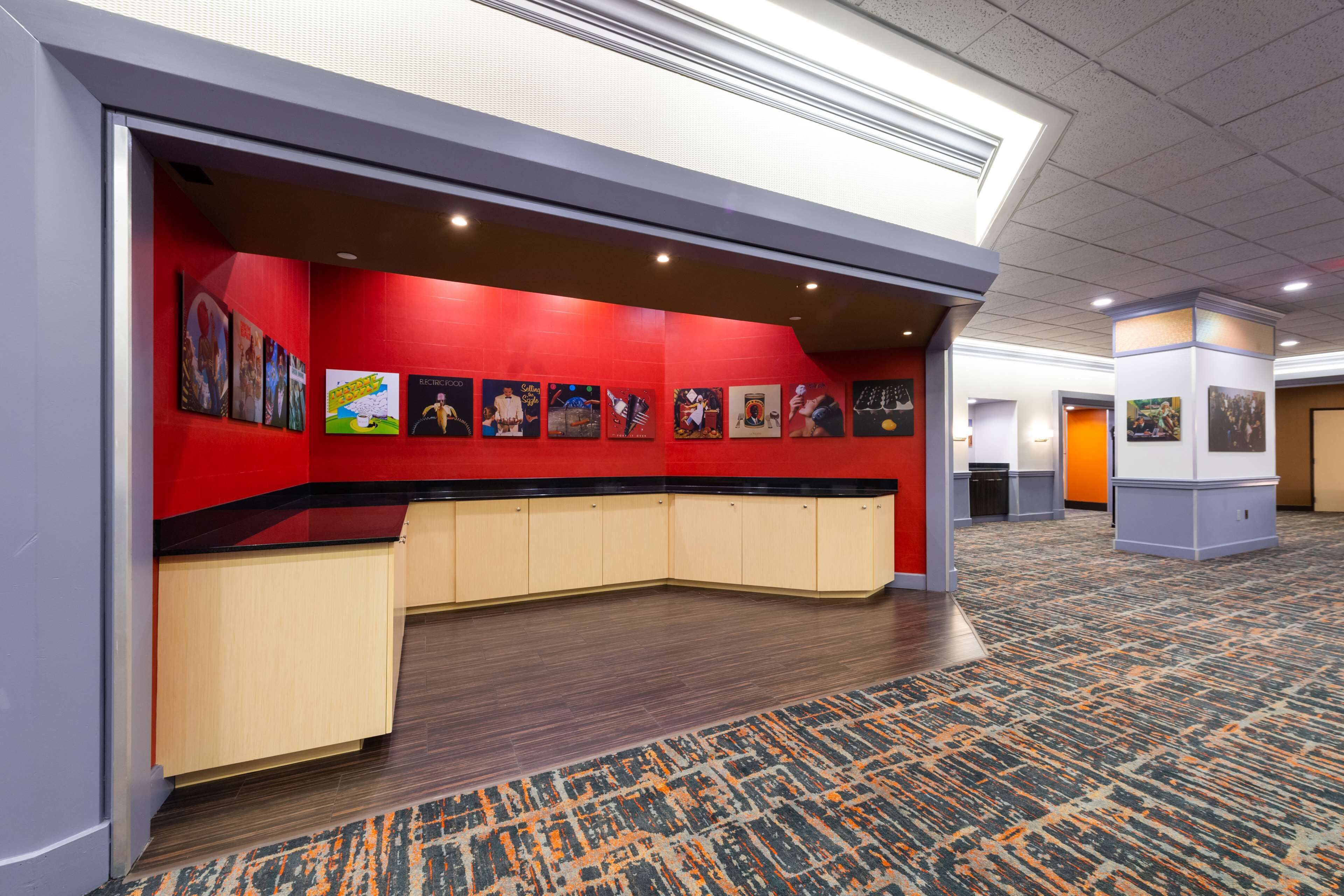 A hotel lobby with a red accent wall, a curved reception desk, and a patterned carpet.