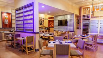 A restaurant with multiple tables and chairs, a wall with a unique design, and a shelf with glasses.