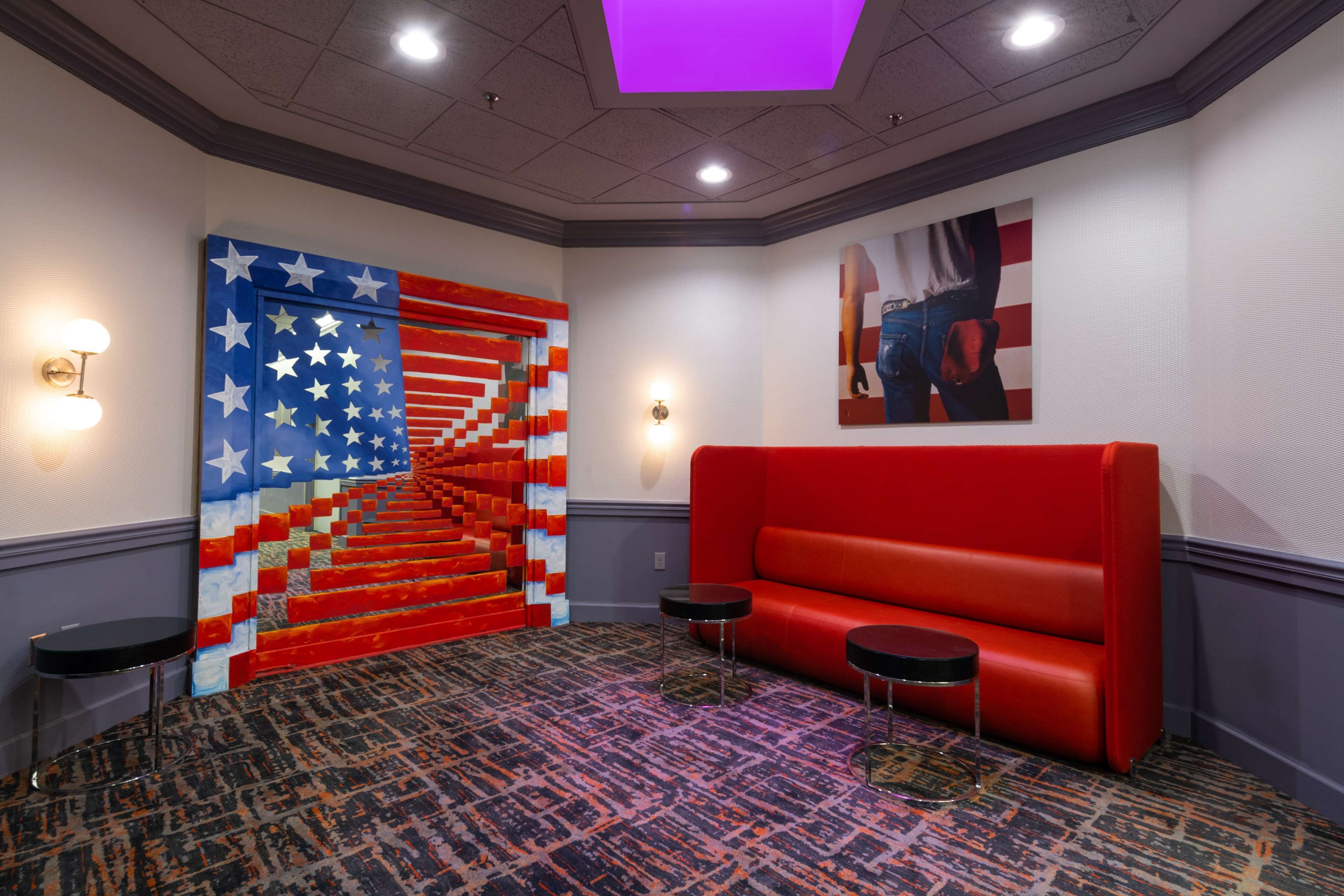 A lobby with a red sofa, two black stools, a patterned carpet, and a wall with a large American flag mural.