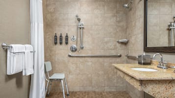 A modern bathroom with a shower, grab bars, a sink, and a chair.