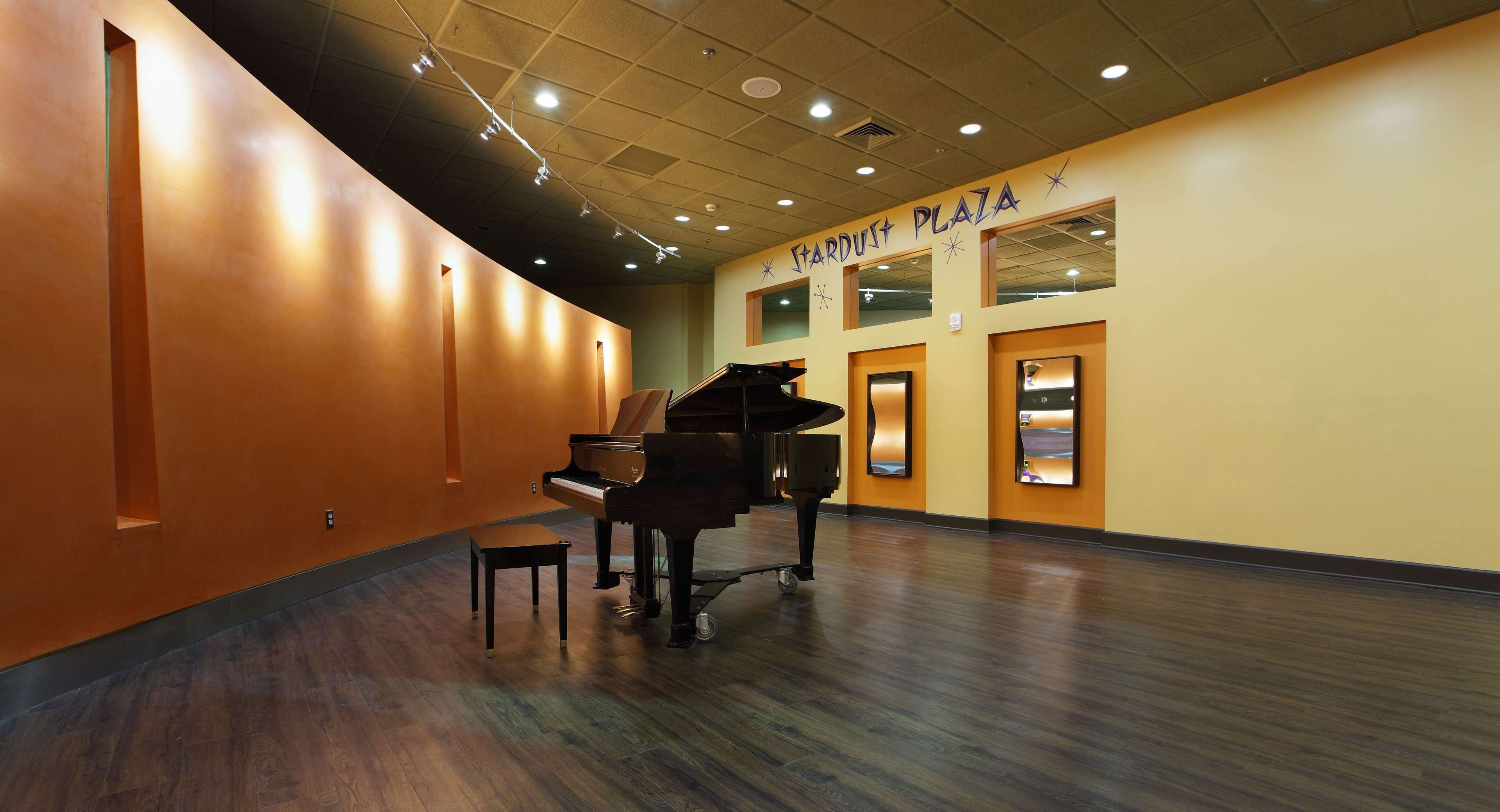 A spacious hallway with a grand piano and a small stool, leading to a room with a large window and a sign reading "CARDUST PLAZA".