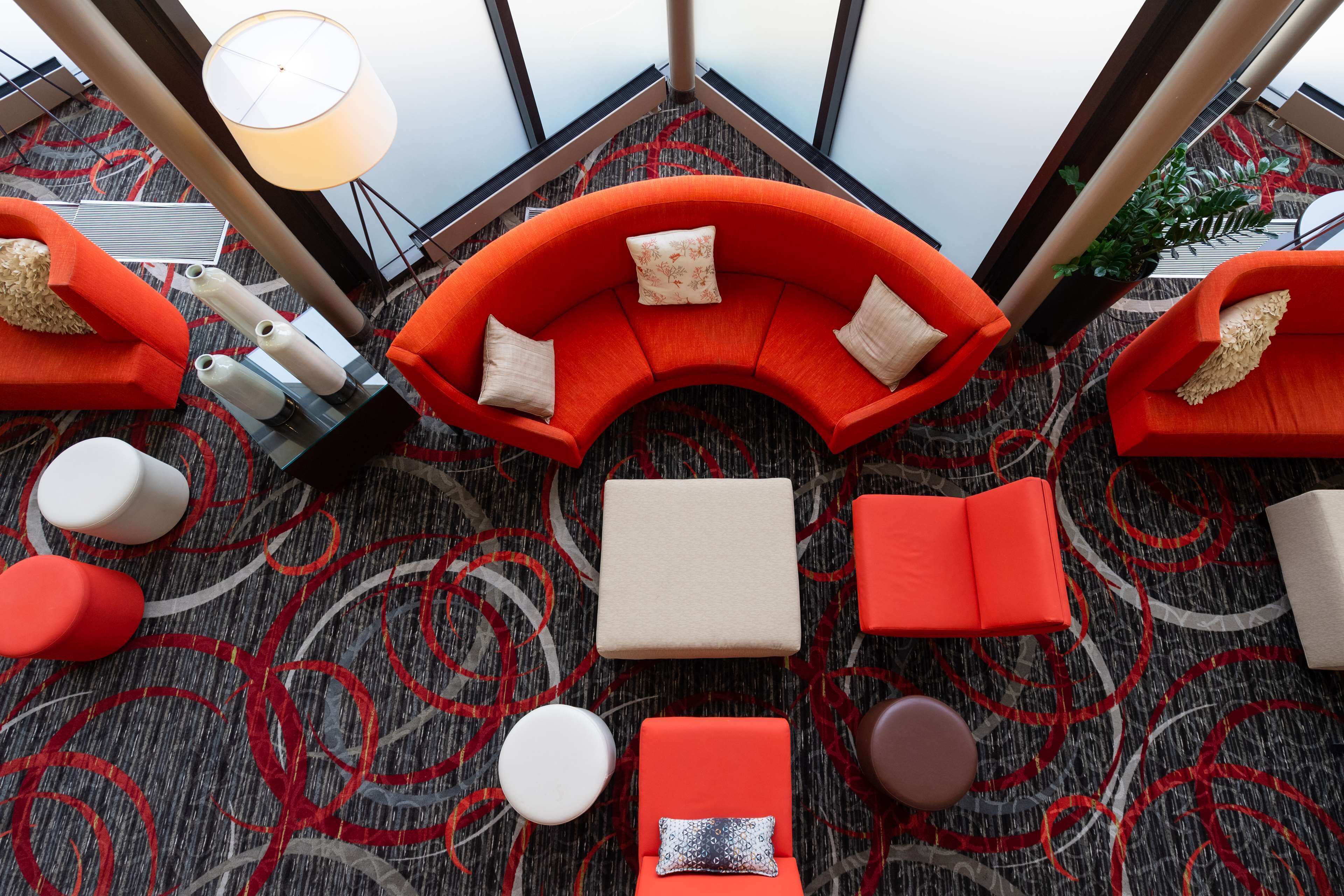 A modern lounge area with a curved orange sofa, multiple seating options, and a patterned carpet.