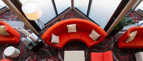Eine moderne Lounge mit einer gebogenen, orangefarbenen Couch, verschiedenen Sitzgelegenheiten und einem gemusterten Teppich.