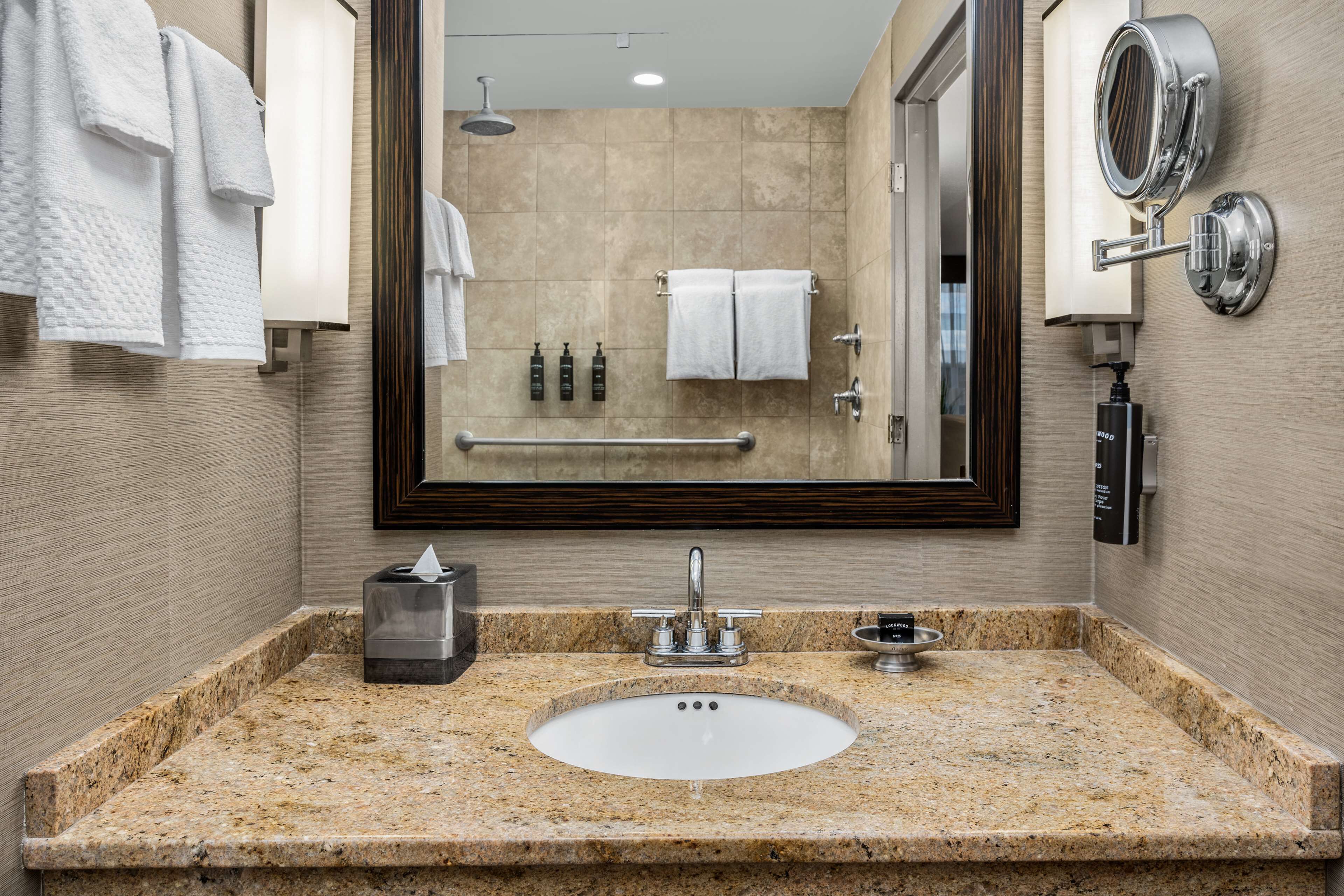 Un baño con lavamanos de encimera de granito, un espejo grande y un perchero para toallas.