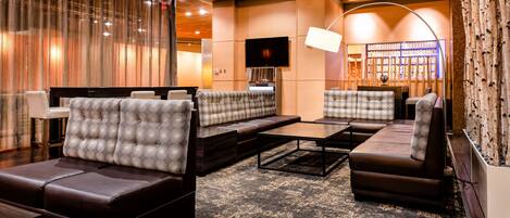 A modern lounge area with leather sofas, a flat-screen TV, and a bar area with bottles.