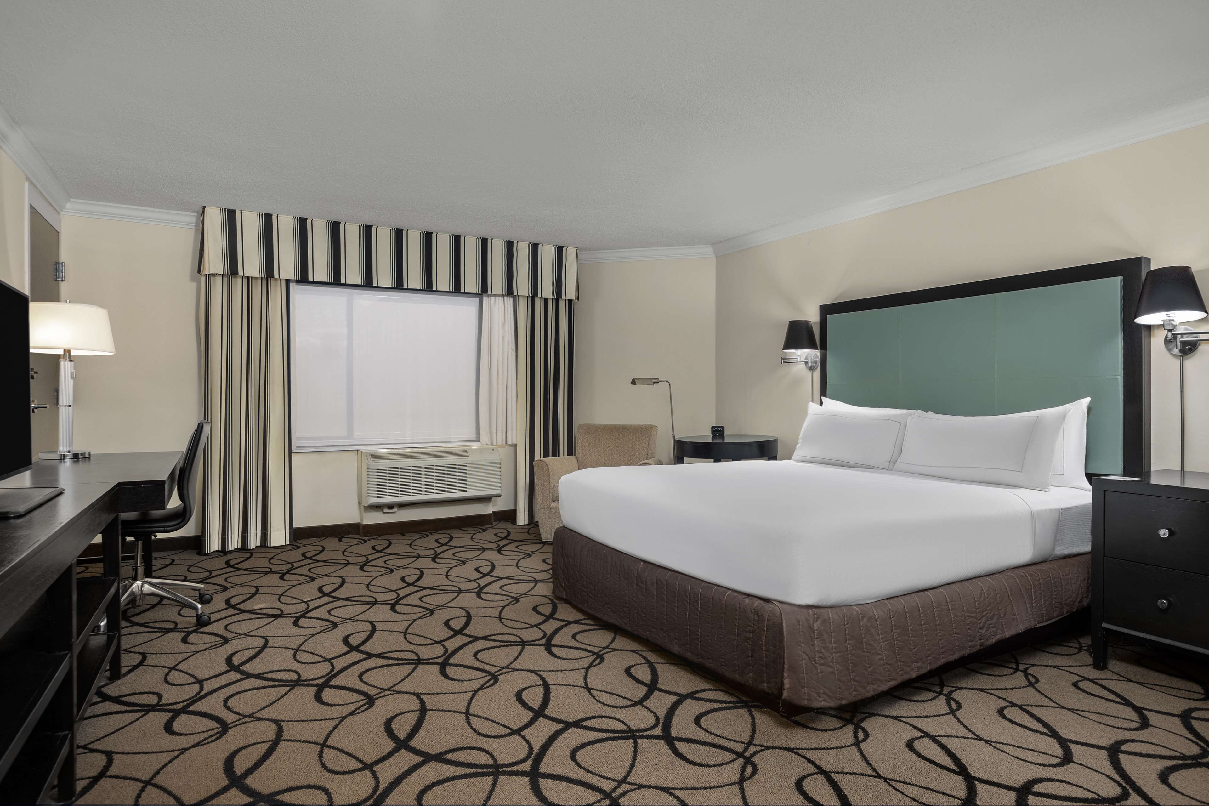 A hotel room with a large bed, a desk with a chair, a TV, and a window with curtains.