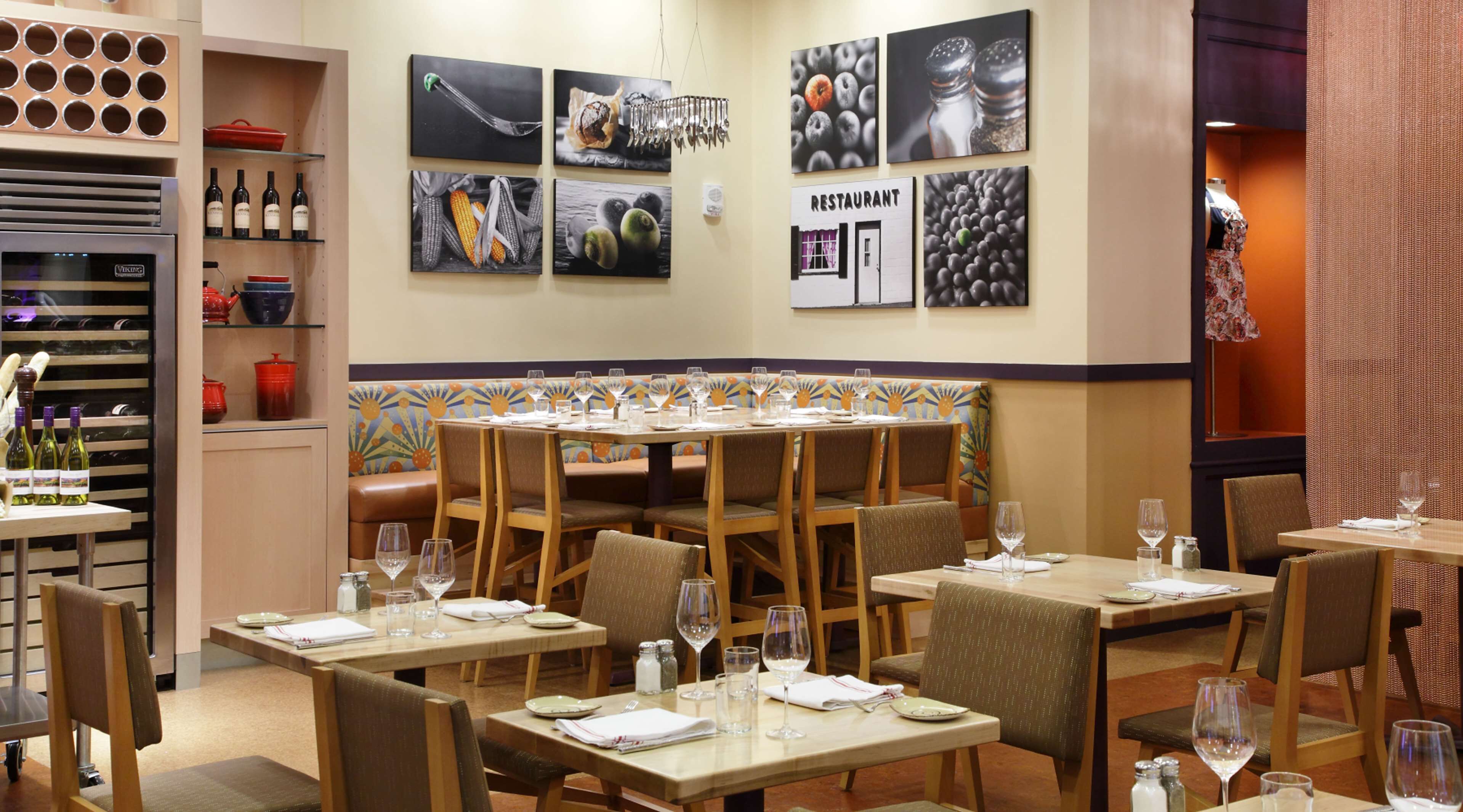 A restaurant interior with multiple dining tables, chairs, and a wall decorated with food-themed artwork.
