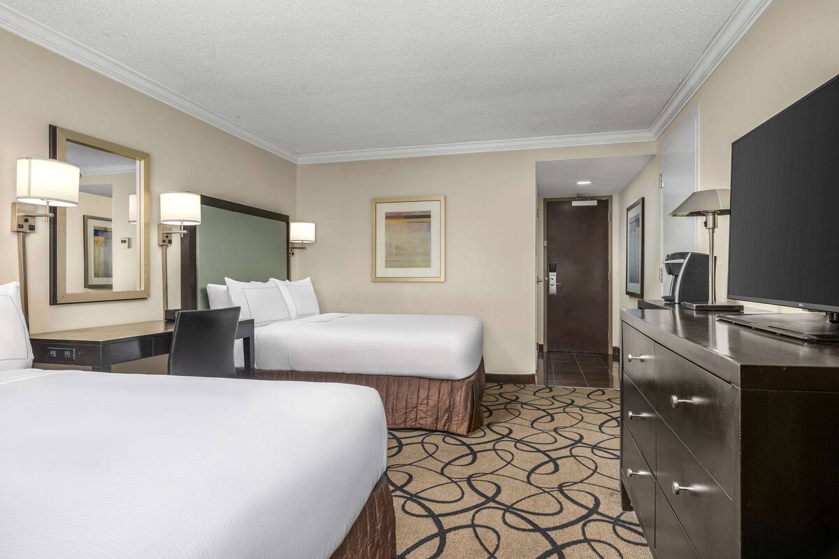 A hotel room with two beds, a dresser, a television, and a framed artwork on the wall.