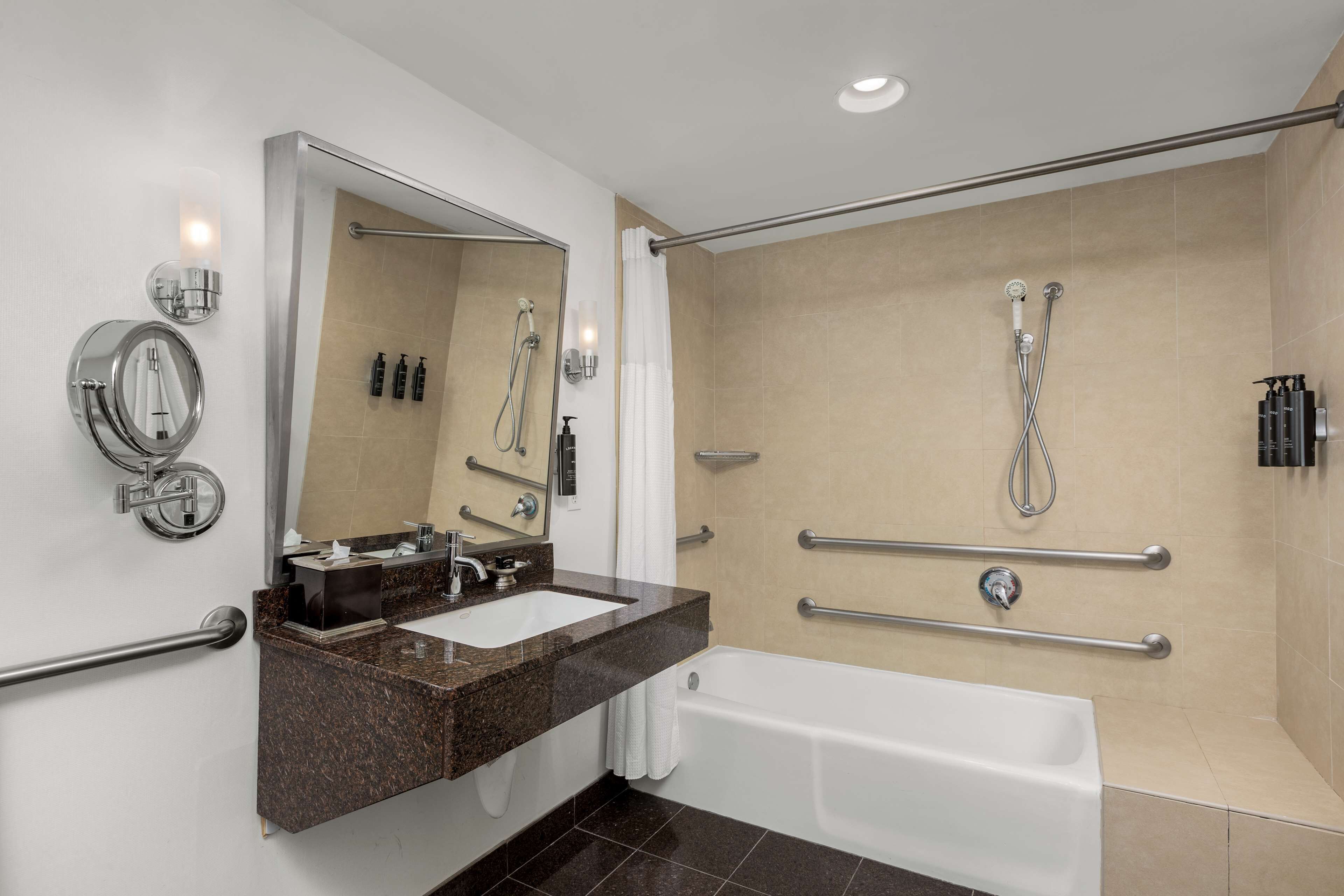 A modern bathroom with a sink, mirror, and bathtub. It includes grab bars and a shower with a handheld showerhead.