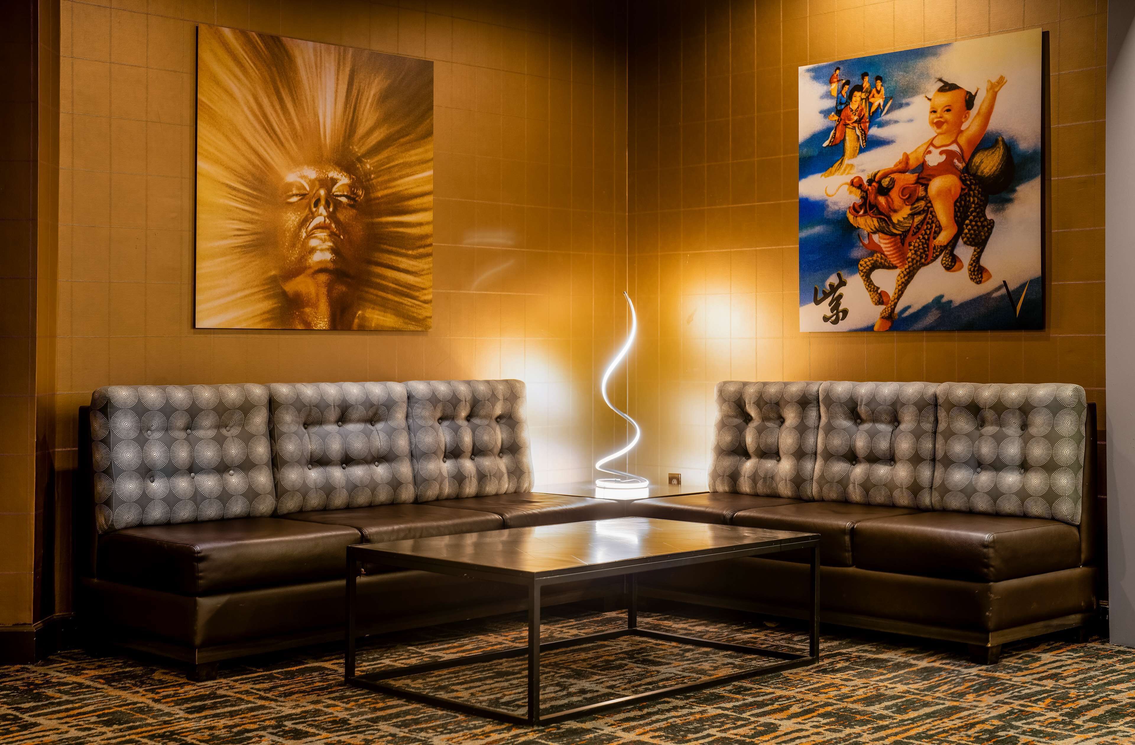 A lobby with two grey tufted sofas, a glass coffee table, and two large wall paintings.