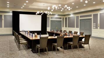 A conference room with a long table, chairs, a projector screen, and a chandelier.