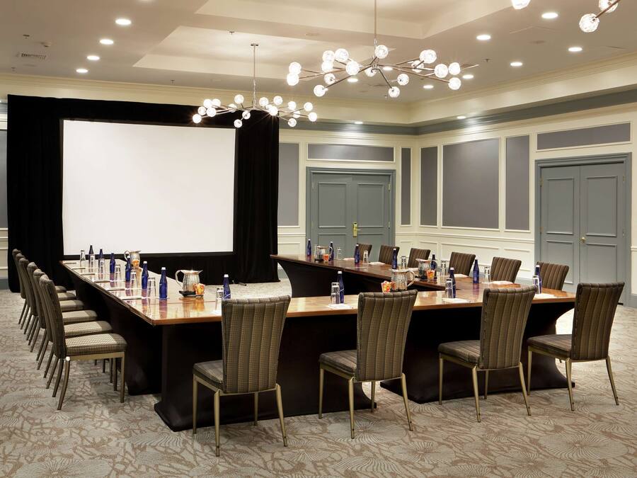 A conference room with a long table, chairs, a projector screen, and a chandelier.
