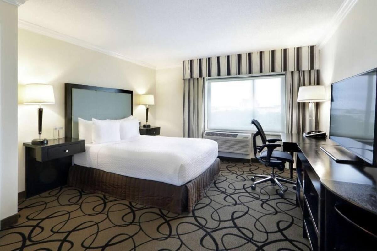 A hotel room with a bed, desk, chair, television, and large window.
