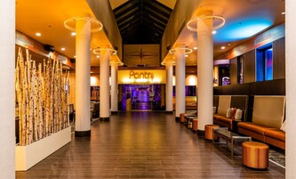 Un vestíbulo de hotel con un restaurante Panera Bread en el centro, muebles modernos y un techo alto con luminarias circulares.