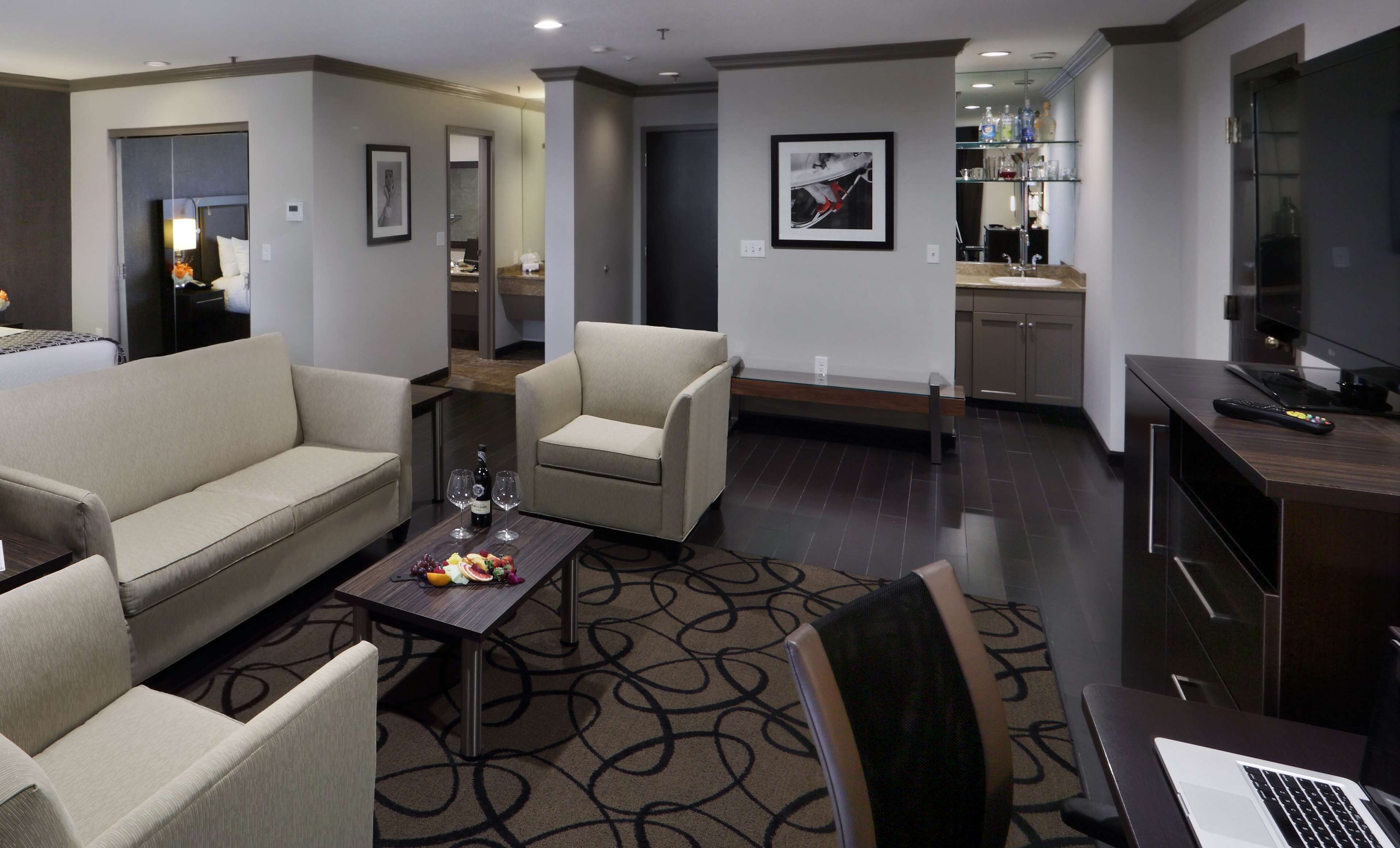 Una habitación de hotel moderna con sofá, sillones, una mesa de centro con fruta, una computadora portátil y un televisor.