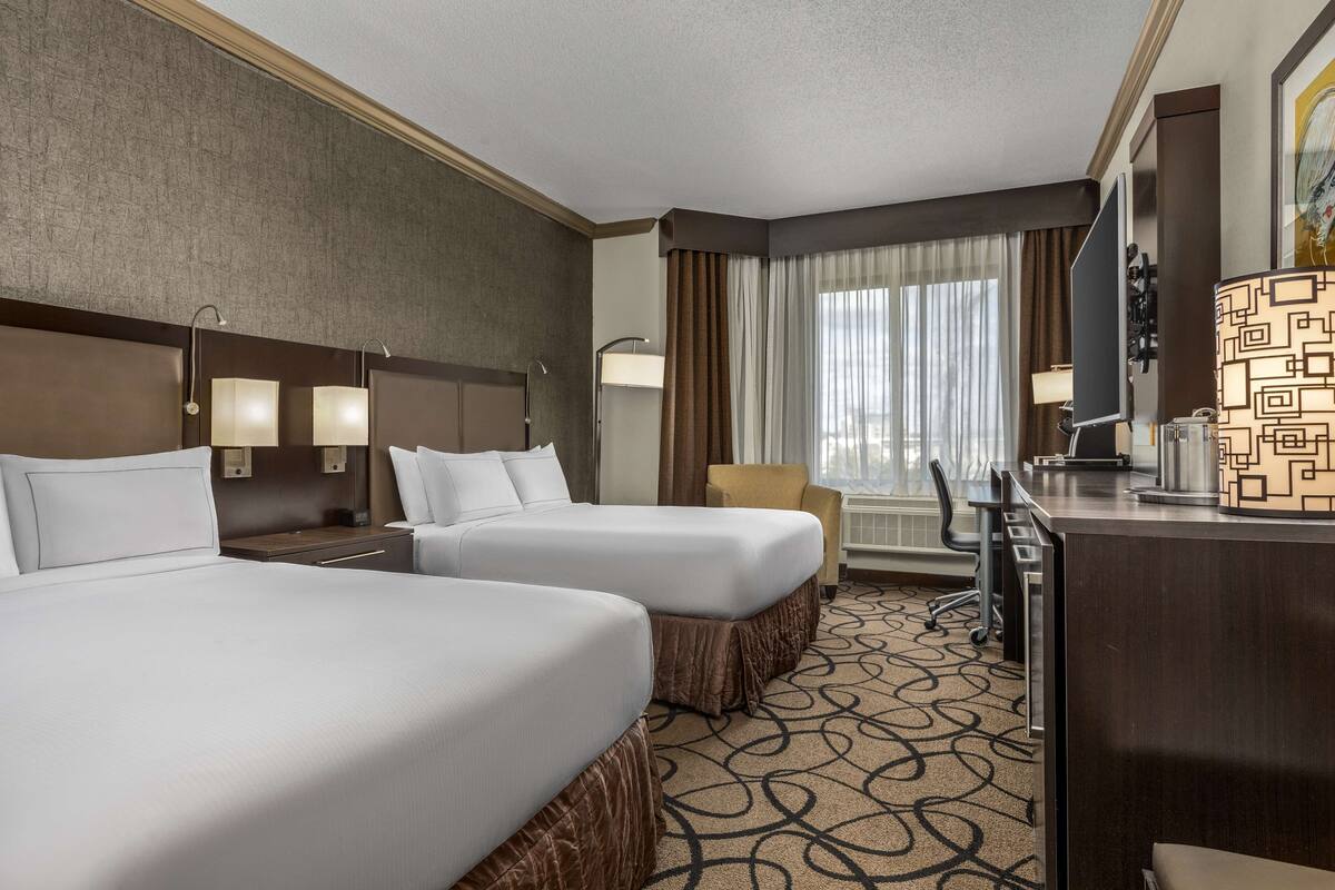 A hotel room with two beds, a desk, a chair, a TV, and a window with curtains.