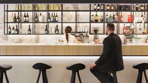 A bar area with a marble countertop, multiple stools, and a variety of bottles and glasses on shelves. - JR Hotels Bologna Gate 7 (Calderara di Reno)