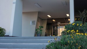 A hotel entrance with steps leading up to a glass door, a potted plant, and yellow flowers in the foreground. - JR Hotels Bologna Gate 7 (Calderara di Reno)