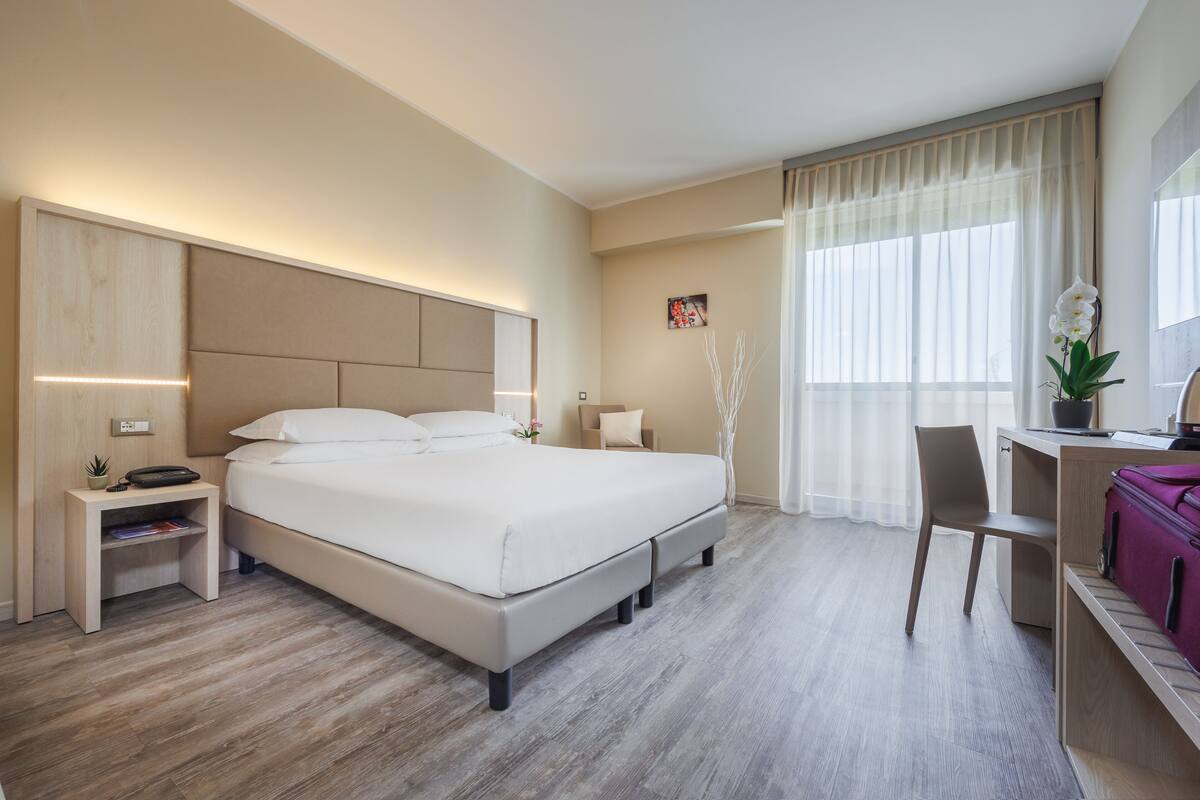 A modern hotel room with a large bed, bedside tables, a desk, and a chair.