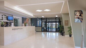 A reception area with a modern design, including a reception desk labeled "RECEPTION," a flat-screen TV, and a glass door entrance. - JR Hotels Bologna Gate 7 (Calderara di Reno)