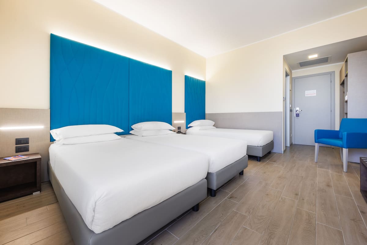A hotel room with two beds, a desk, a chair, and a door.