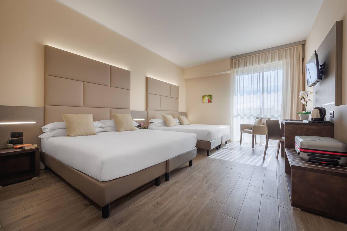 A hotel room with two beds, a desk, a chair, a TV, and a window with curtains.
