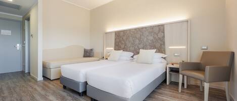 A hotel room with a double bed, a bedside table, a chair, and a sofa.