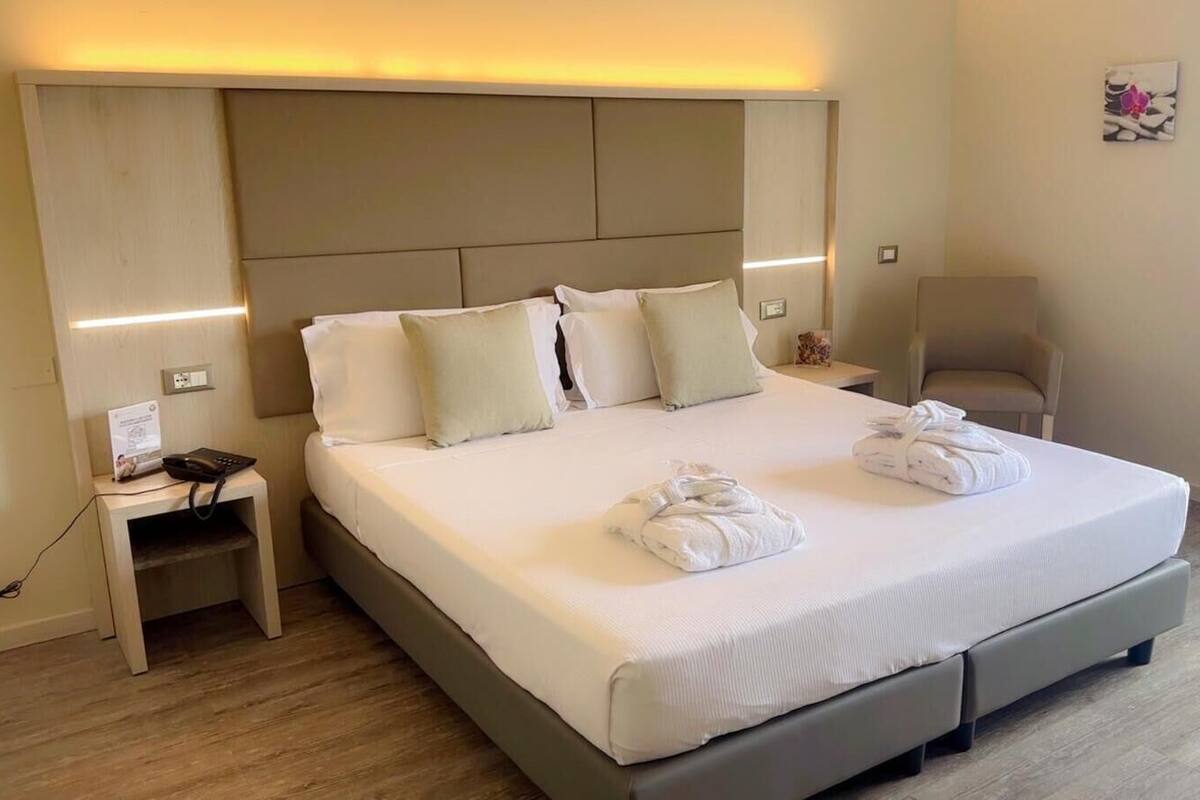 A hotel room with a large bed, two bedside tables, a wall-mounted telephone, and a small bedside lamp.