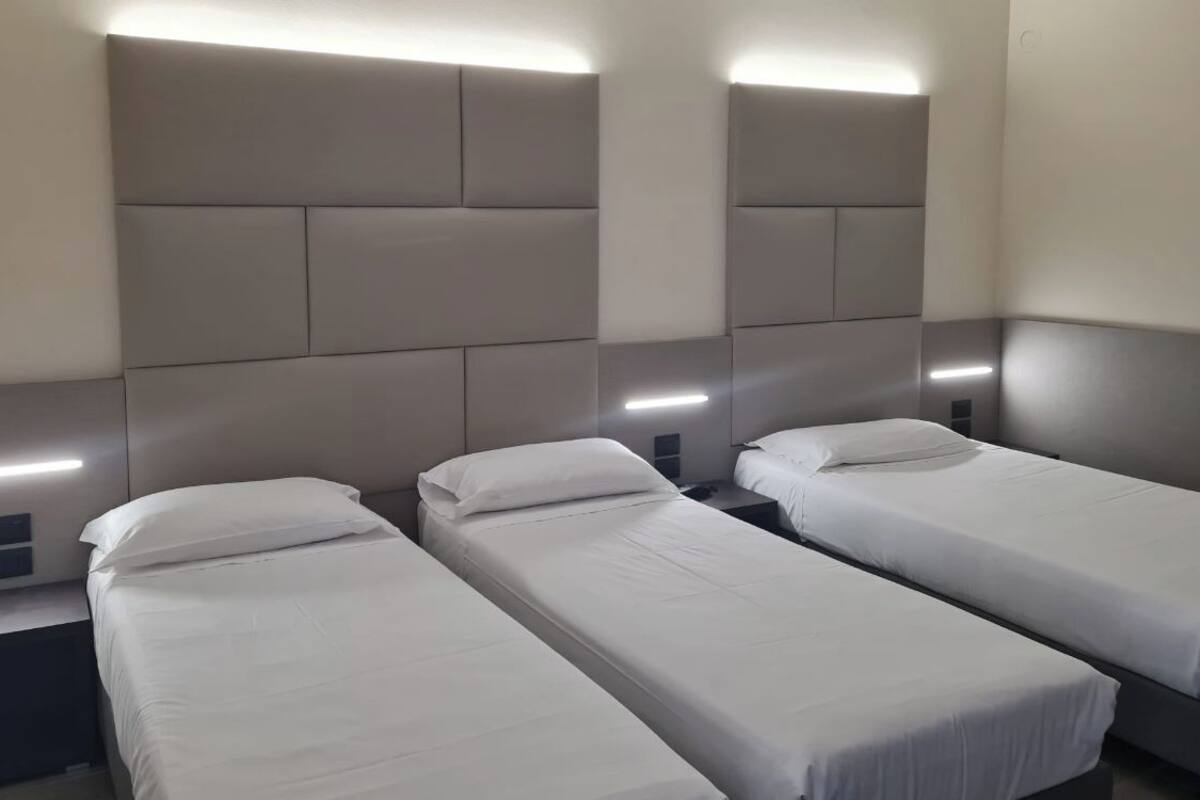 A hotel room with three single beds, each with a headboard and bedside tables.