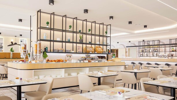 A modern cafe with a central counter, multiple seating areas, and a variety of items on display. - JR Hotels Bologna Gate 7 (Calderara di Reno)