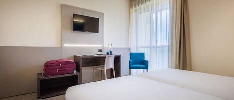 Habitación de hotel con una cama grande, un escritorio con computadora, una silla, televisor montado en la pared y una ventana con cortinas.