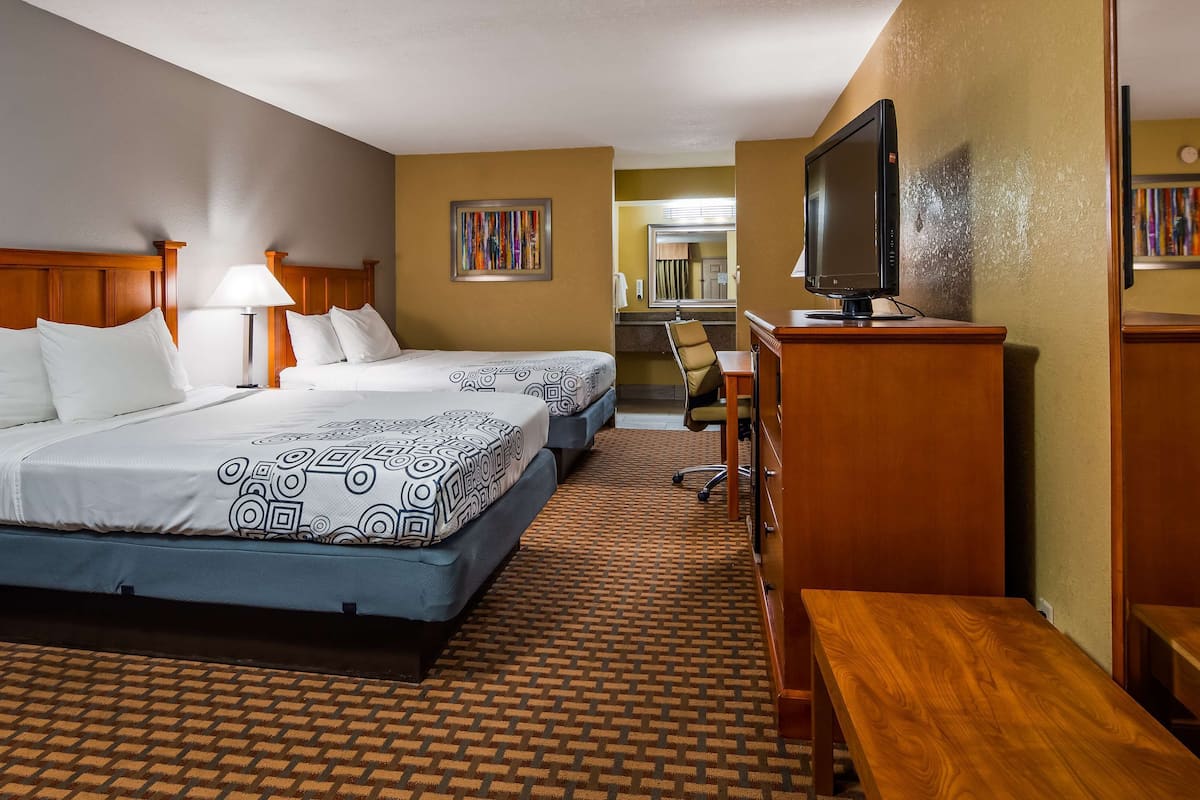 A hotel room with two beds, a desk, a television, and a bathroom visible in the background.