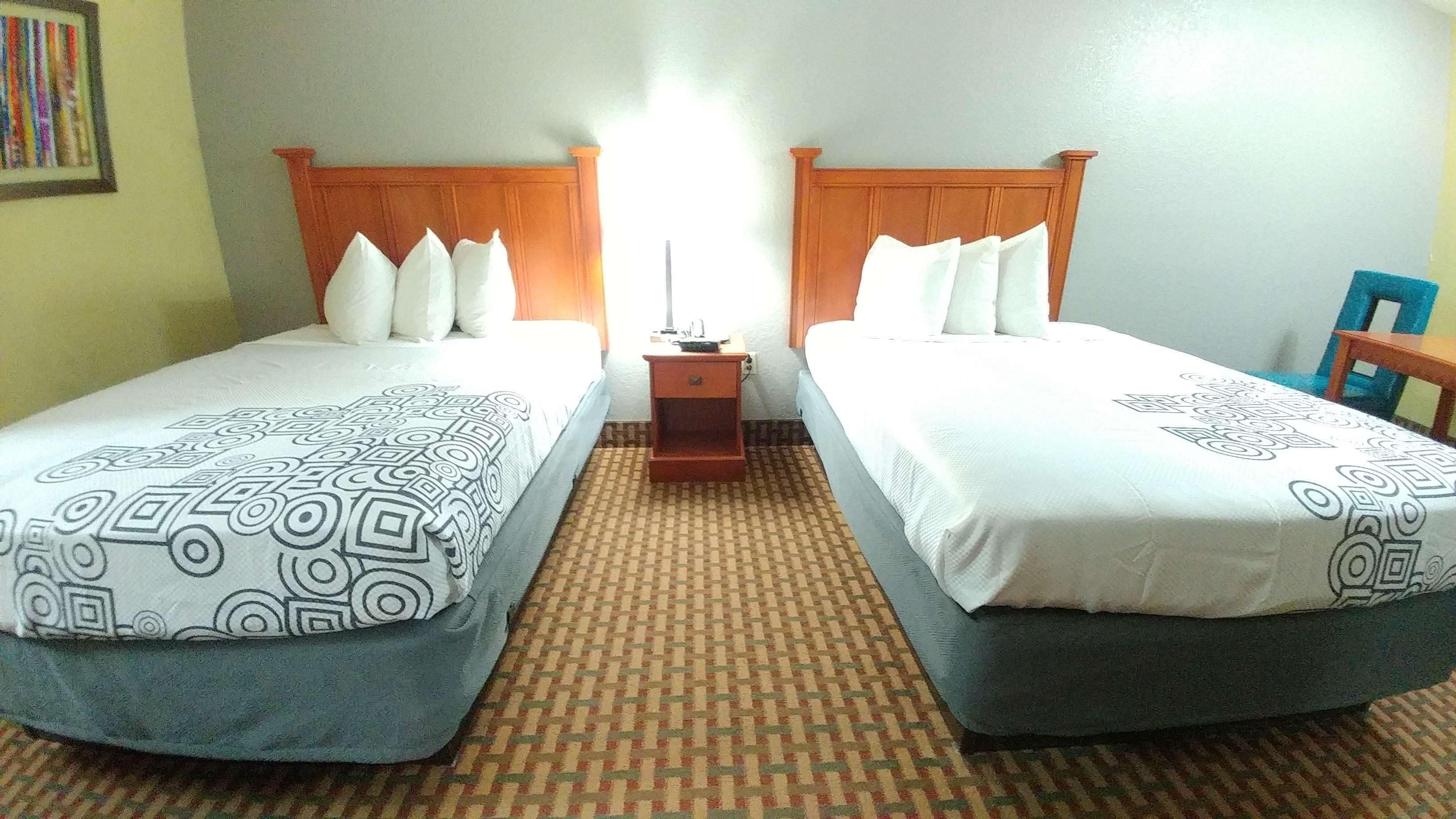 Una habitación de hotel con dos camas, una mesita de noche y una silla.