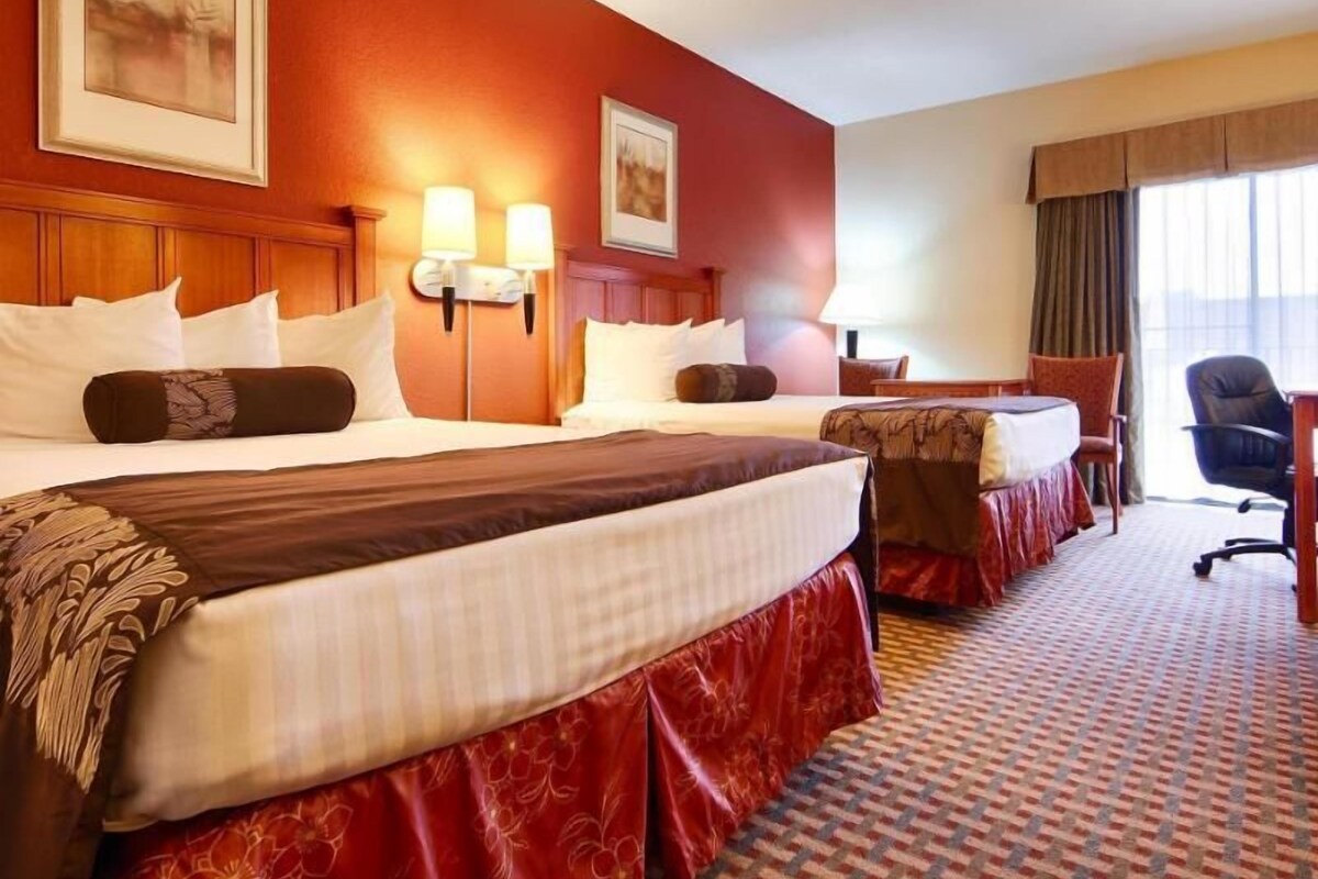 A hotel room with two beds, a desk, a chair, and a large window.