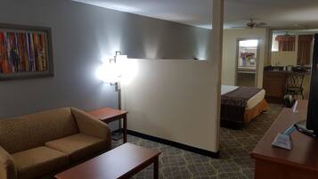 Habitación de hotel con sofá, una pequeña mesa, cama, escritorio, lámpara, ventilador de techo y zona de cocina.