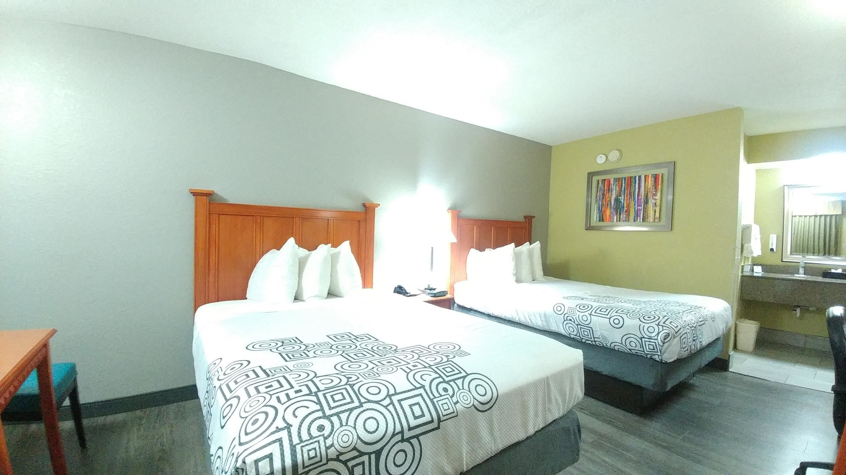 Habitación de hotel con dos camas, un escritorio y un baño.
