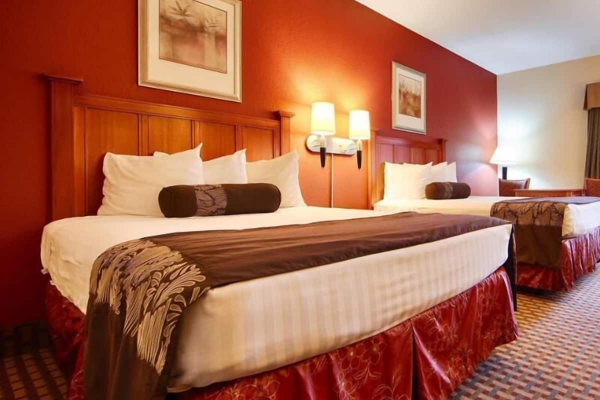 A hotel room with two beds, wooden headboards, wall-mounted lamps, and a patterned carpet.