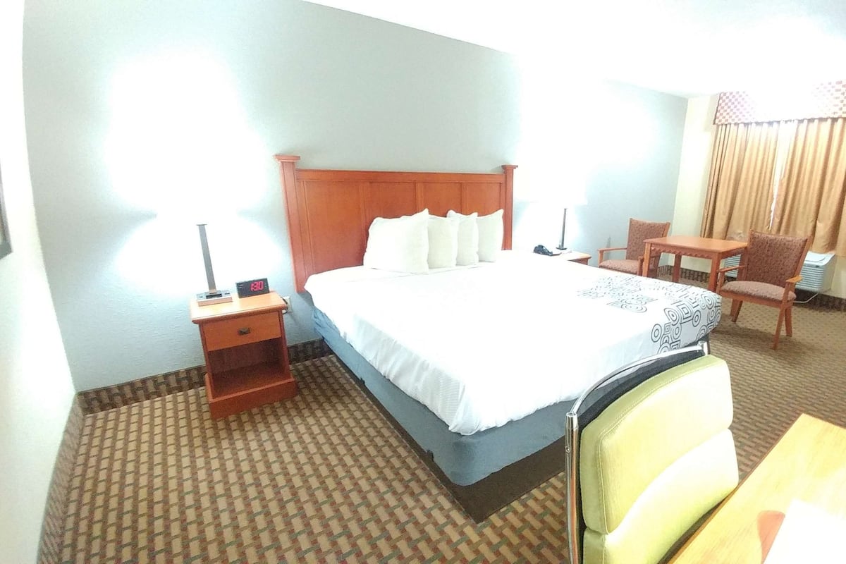 A hotel room with a bed, a desk, a chair, and a small table.