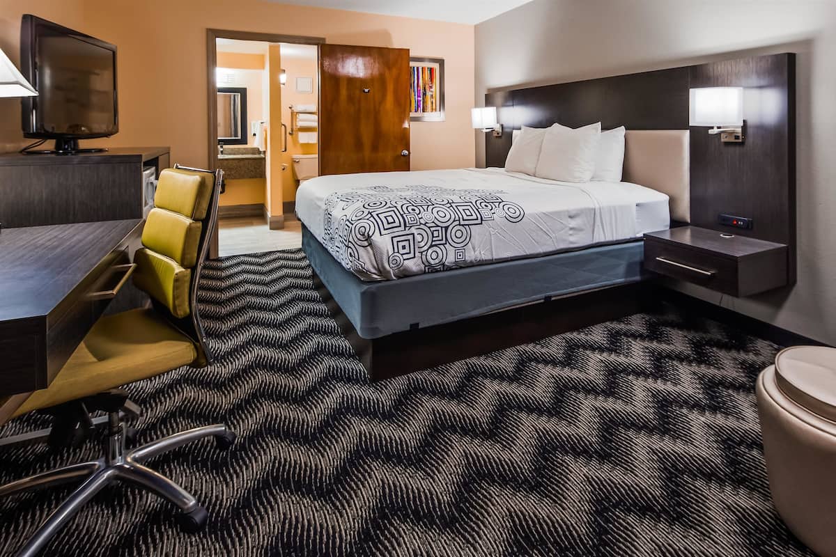 A hotel room with a bed, desk, chair, and a bathroom visible through an open door.