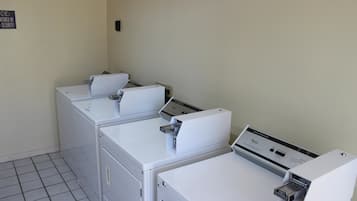 A laundry room with three stacked washers and dryers, a sign indicating security monitoring, and a tiled floor.