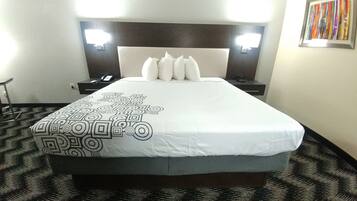 A hotel room with a large bed, a headboard with lights, a desk with a phone, and a wall with a colorful artwork.