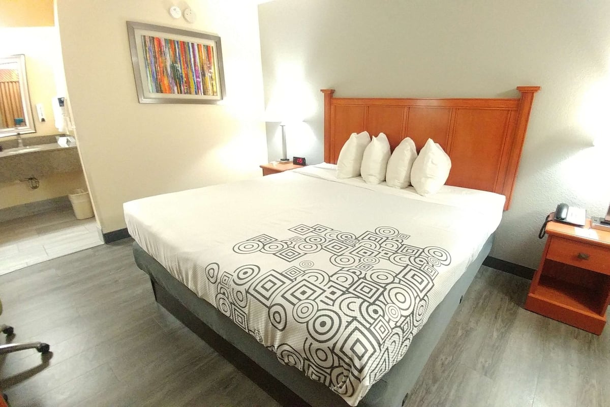 A hotel room with a bed, bedside tables, a mirror, a clock, and a painting on the wall.