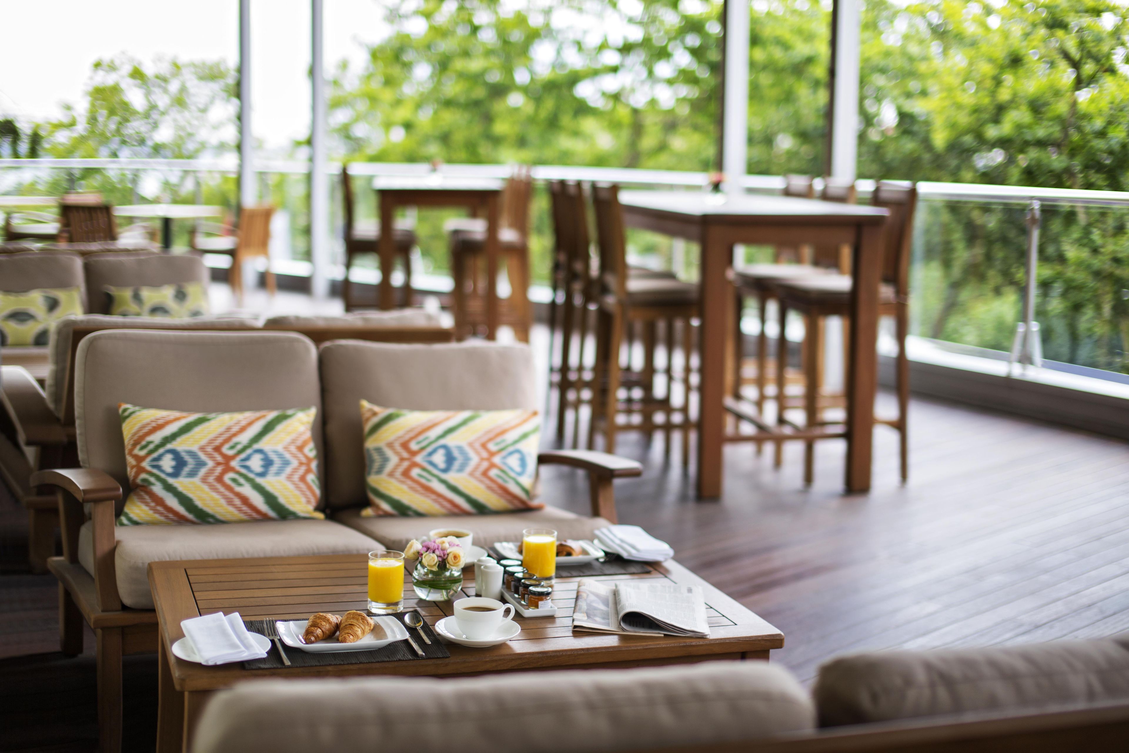A dining area with wooden furniture, a table set with breakfast items, and a view of greenery outside.